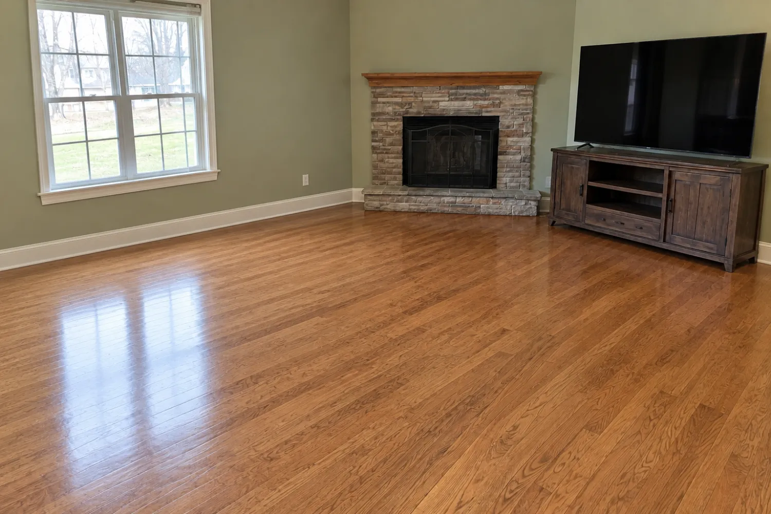 The same living room emptied to the hardwood floor, with the stone corner fireplace, the window and the TV on its wooden stand still in place