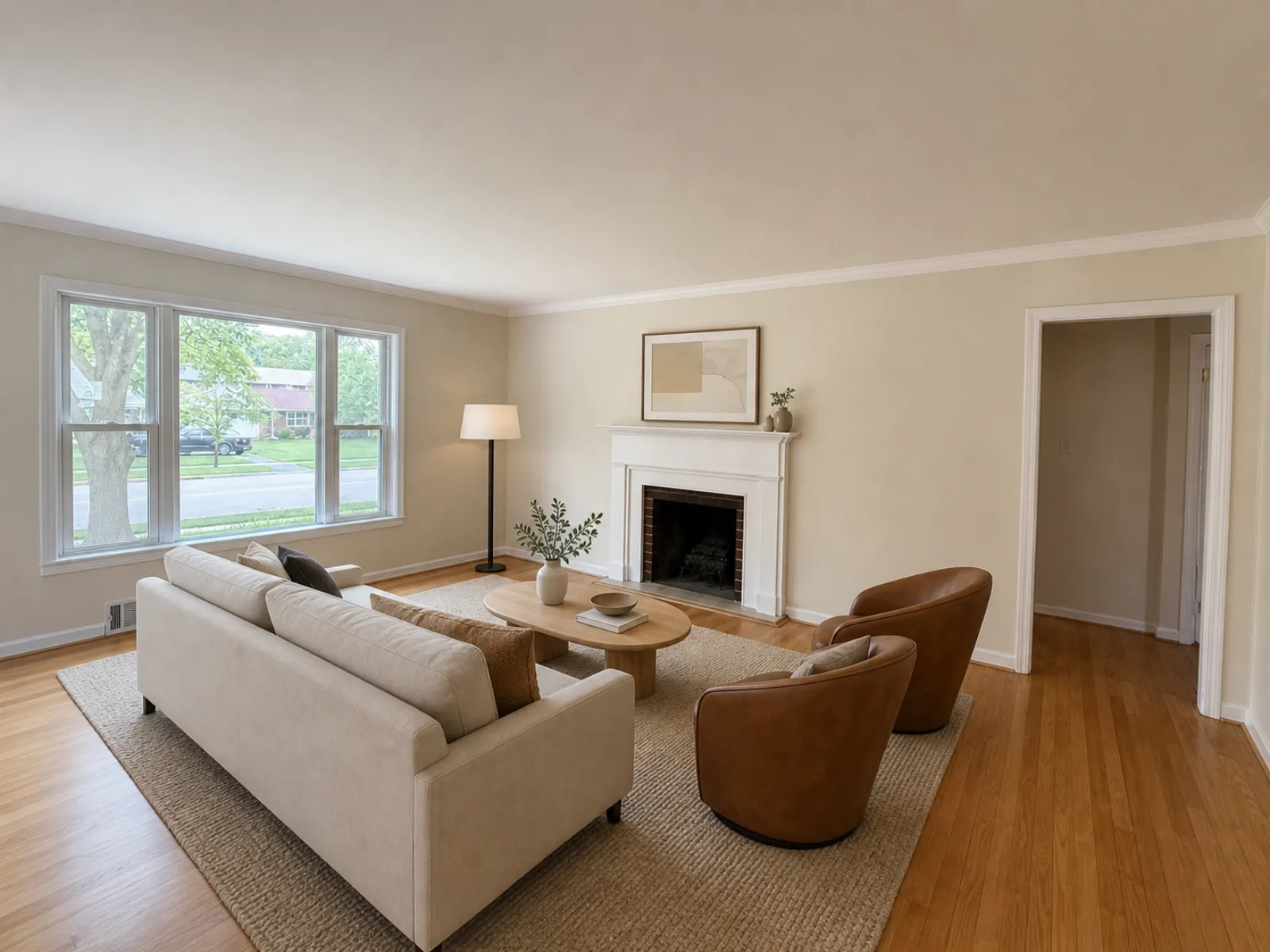 The same living room virtually staged with a cream sofa, two brown leather swivel chairs, an oval wood coffee table, a jute rug and a floor lamp