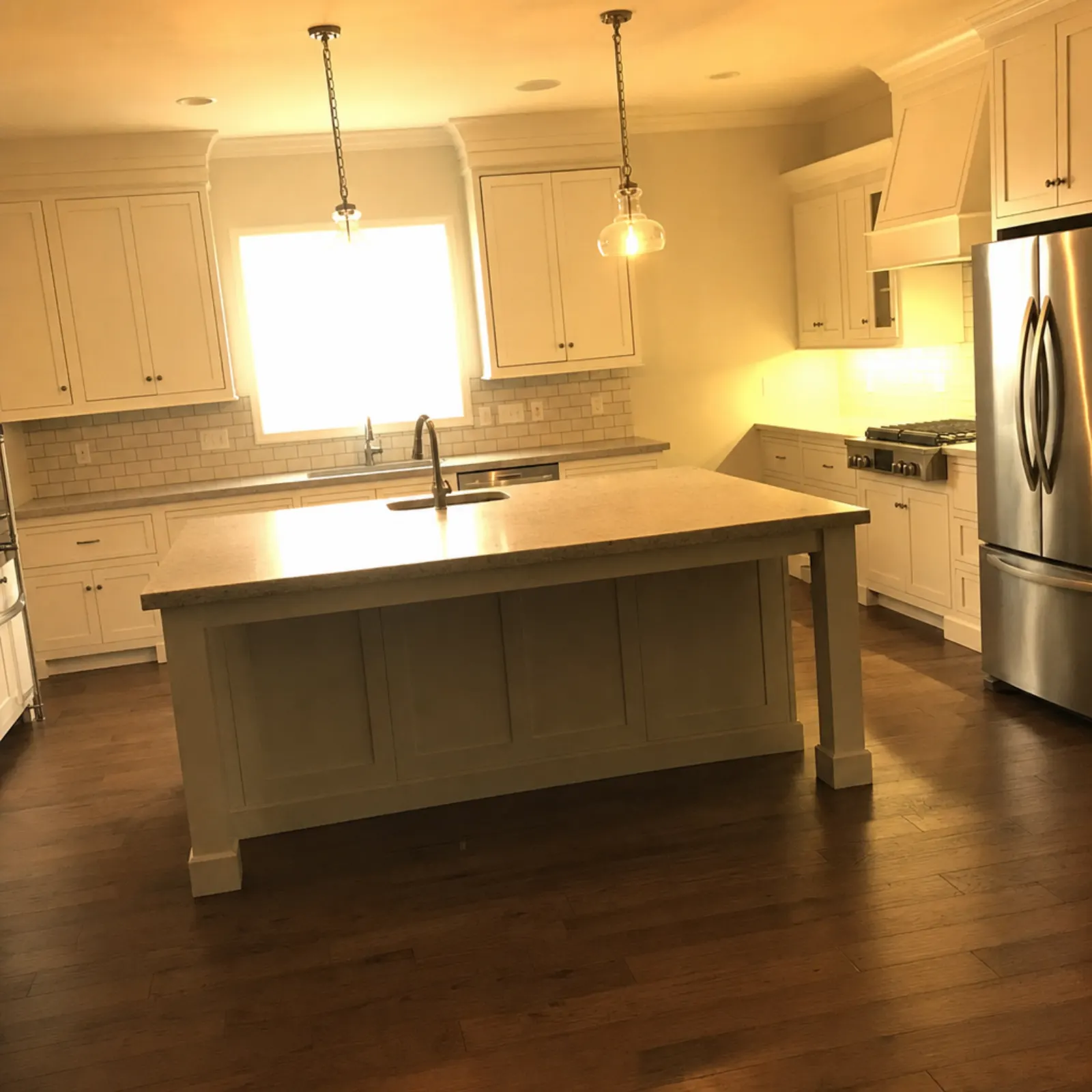 Kitchen with white shaker cabinets and a large island, a heavy yellow-orange color cast, a dark floor and the window over the sink blown out to solid white